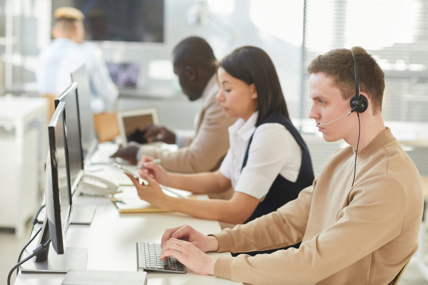 Young people wearing headsets sitting in row while working in call center